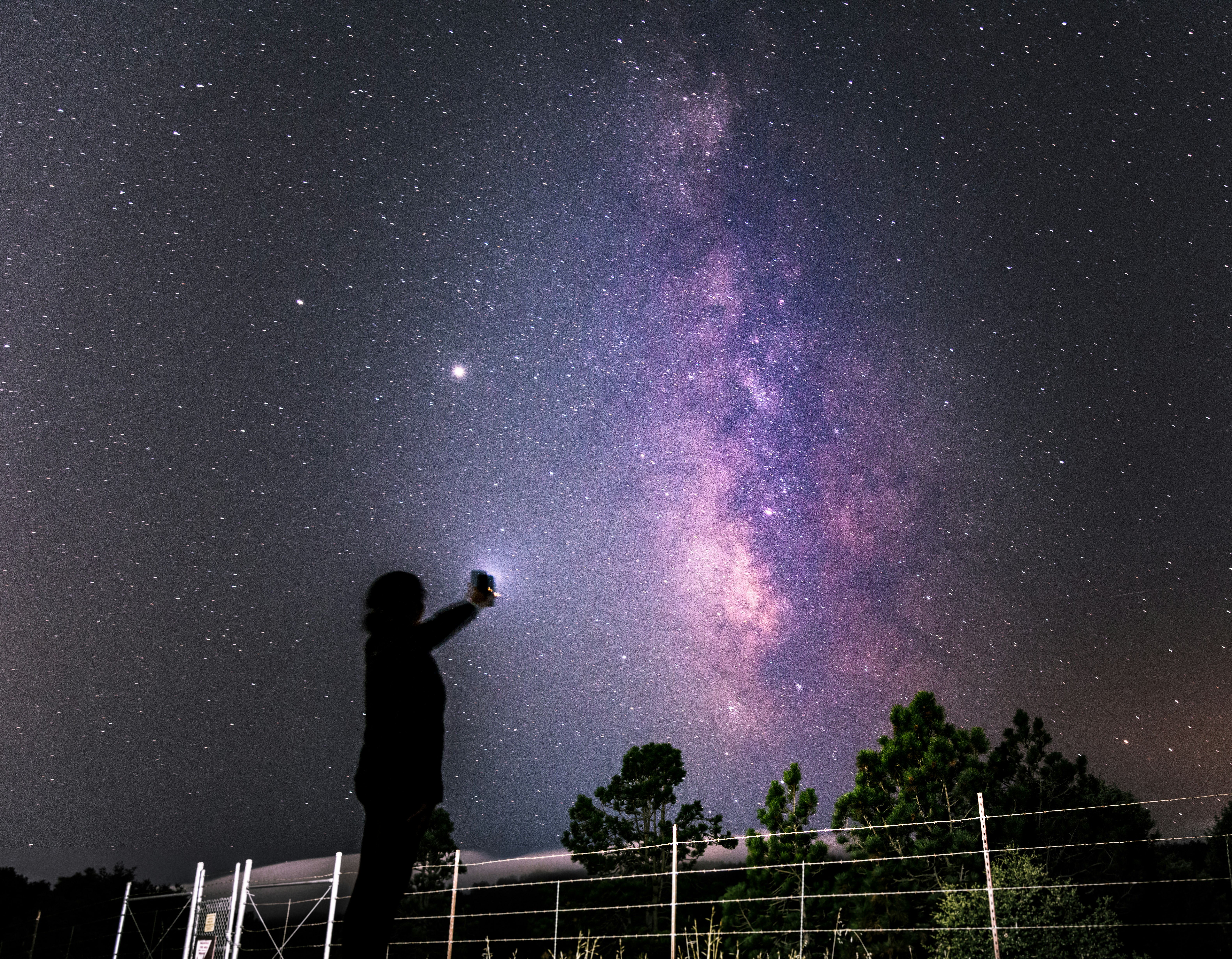 silhouette of man standing on fence under starry night